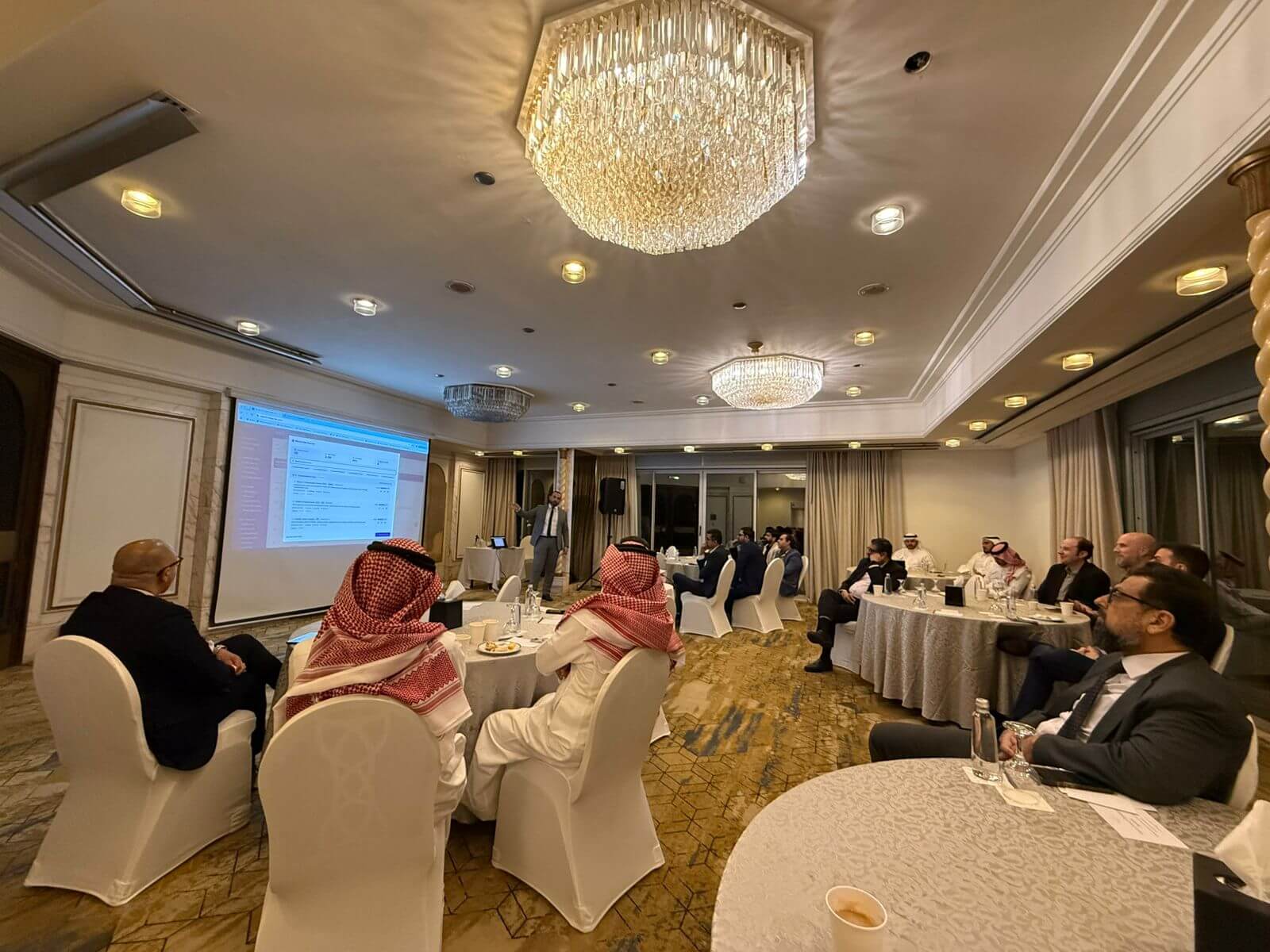 Senior leaders gathered around tables in a Jeddah ballroom for the THΔKΔA executive dinner, watching a live AI demonstration.